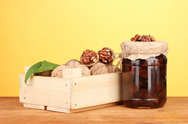 Jam-jar de nozes e caixa de madeira no fundo laranja — Fotografia de Stock