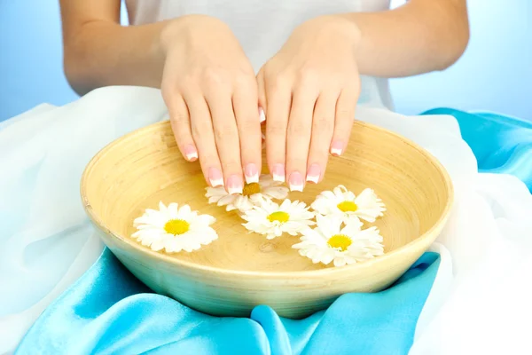 Manos de mujer con cuenco de madera de agua con flores, sobre fondo azul — Foto de Stock