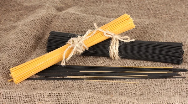 Black and yellow spaghetti on sackcloth background — Stock Photo, Image