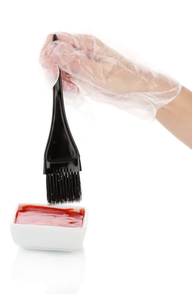 Γυναίκας χέρι σε ένα γάντι βυθίζει το πινέλο σε προϊόντα βαφής μαλλιών, σε λευκό φόντο — Φωτογραφία Αρχείου