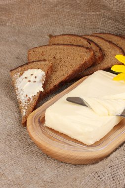 Ahşap kutusunda ekmek ve backgrou çuval bezi üzerinde çiçekler çevrili tereyağı