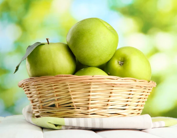 Ripe green apples with leaves in basket, on wooden table, on window backgro — Stock Photo, Image