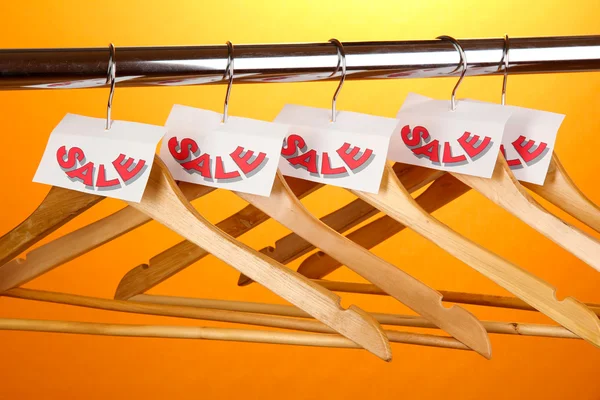 Wooden clothes hangers as sale symbol on orange background — Stock Photo, Image