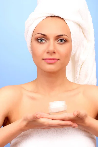 Mooie jonge vrouw na douche met een handdoek op haar hoofd en een pot van cr — Stockfoto