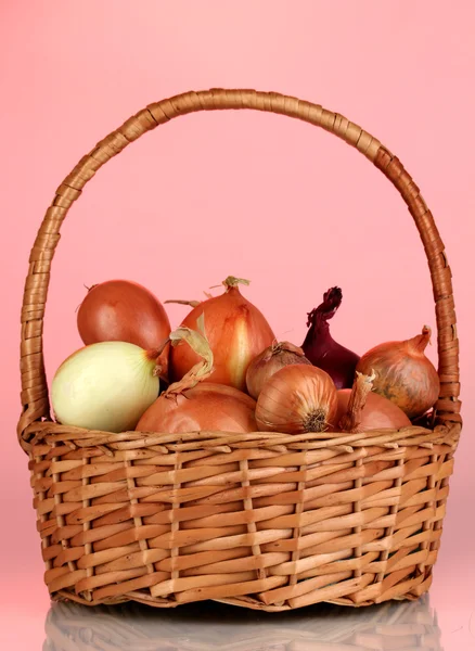 Reife Zwiebeln im Korb auf rotem Hintergrund — Stockfoto