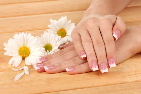 Woman hands with french manicure and flowers on wooden background