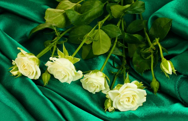 Wunderschöne weiße Rosen auf grünem Satin in Nahaufnahme — Stockfoto