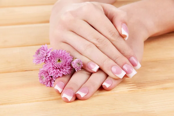 Kvinna händer med fransk manikyr och blommor på trä bakgrund — Stockfoto