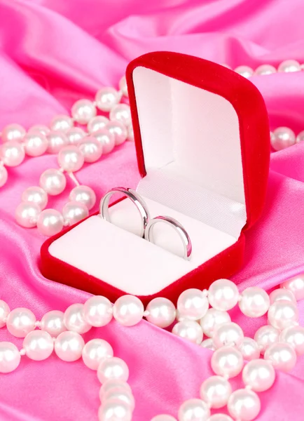 Anillos de boda en caja roja sobre fondo de tela rosa — Foto de Stock