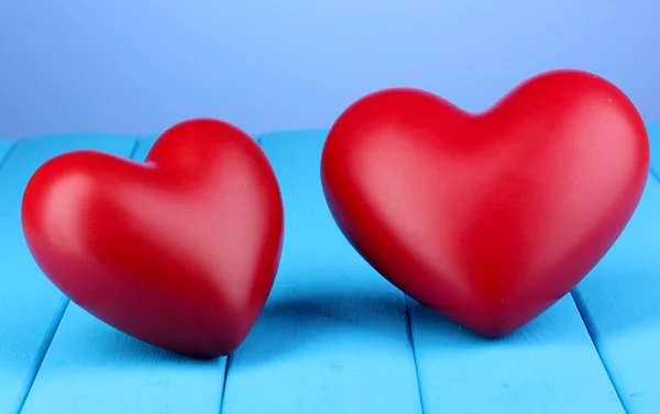 Coeurs rouges décoratifs sur table en bois bleu sur fond bleu — Photo