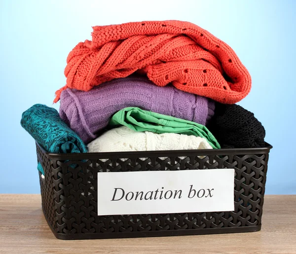 Donation box with clothing on blue background close-up — Stock Photo, Image