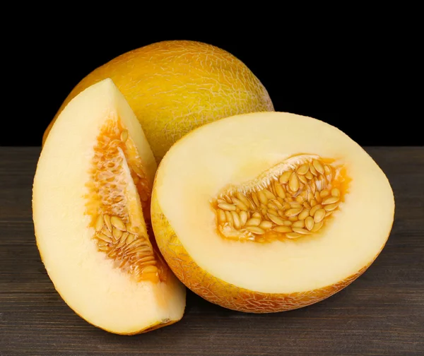 Cut ripe melons on wooden table on black background — Stock Photo, Image