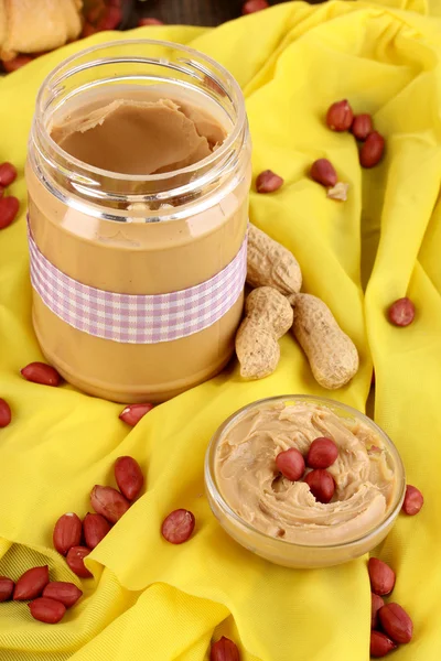 Delicious peanut butter in jar with baking on napkin on wooden table close- — Stock Photo, Image