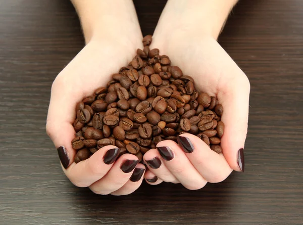 Vrouwelijke handen met koffiebonen, op houten achtergrond — Stockfoto