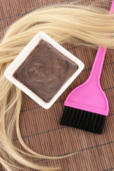 Hair dye in bowl and brush for hair coloring on brown bamboo mat, close-up Stock Picture