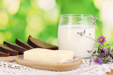 Doğal arka planda ekmek ve sütle çevrili ahşap tutacağa tereyağı.