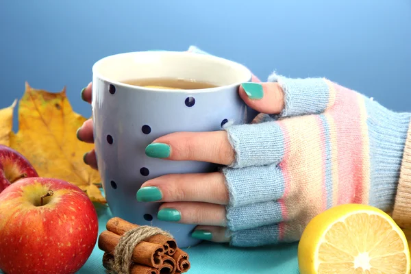 Mani che tengono tazza di bevanda calda e foglie autunnali, su sfondo blu — Foto Stock