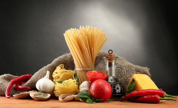 Pasta spaghetti, vegetables and spices, on wooden table, on grey background