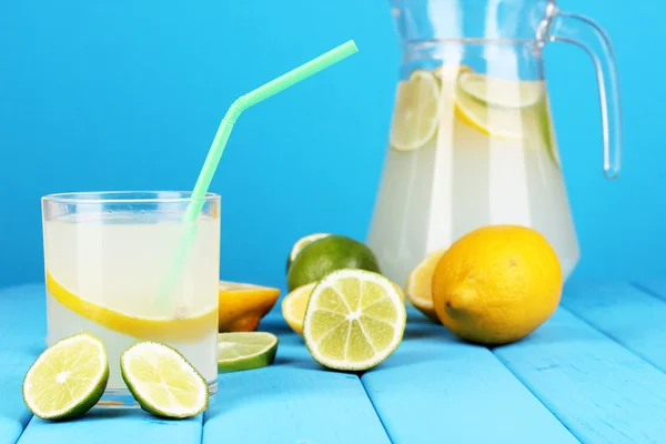 Limonada cítrica en jarra y vaso de cítricos alrededor en mesa de madera en bl —  Fotos de Stock