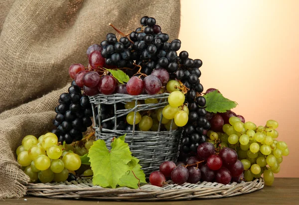 Assortment of ripe sweet grapes in basket, on brown background — Stock Photo, Image