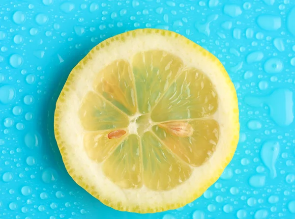 Slice of lemon with drop on blue background — Stock Photo, Image