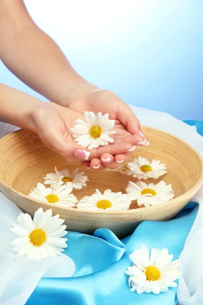 Mains de femme avec bol en bois d'eau avec des fleurs, sur fond bleu — Photo