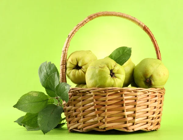 Sweet quinces with leaves in basket, on green background — Stock Photo, Image