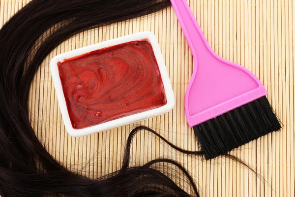 Hair dye in bowl and brush for hair coloring on beige bamboo mat, close-up Stock Image