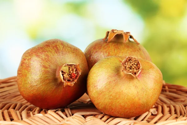 Unripe pomegranates on wicker mat on green background close-up — Stock Photo, Image