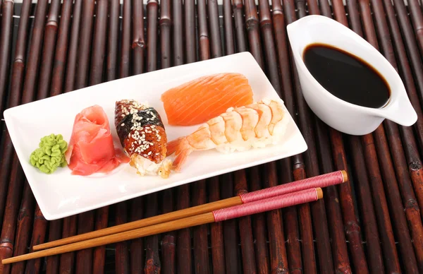 Delicious sushi served on plate on bamboo mat — Stock Photo, Image