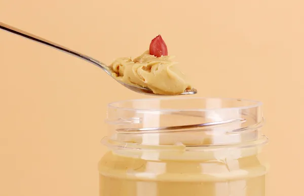 Delicious peanut butter in jar and spoon on beige background — Stock Photo, Image