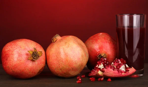 Ripe pomegranates with glass of pomegranate juice on red background — Stock Photo, Image