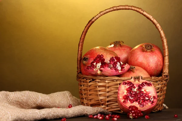 Ripe pomegranates on basket on wooden table on yellow background — Stock Photo, Image