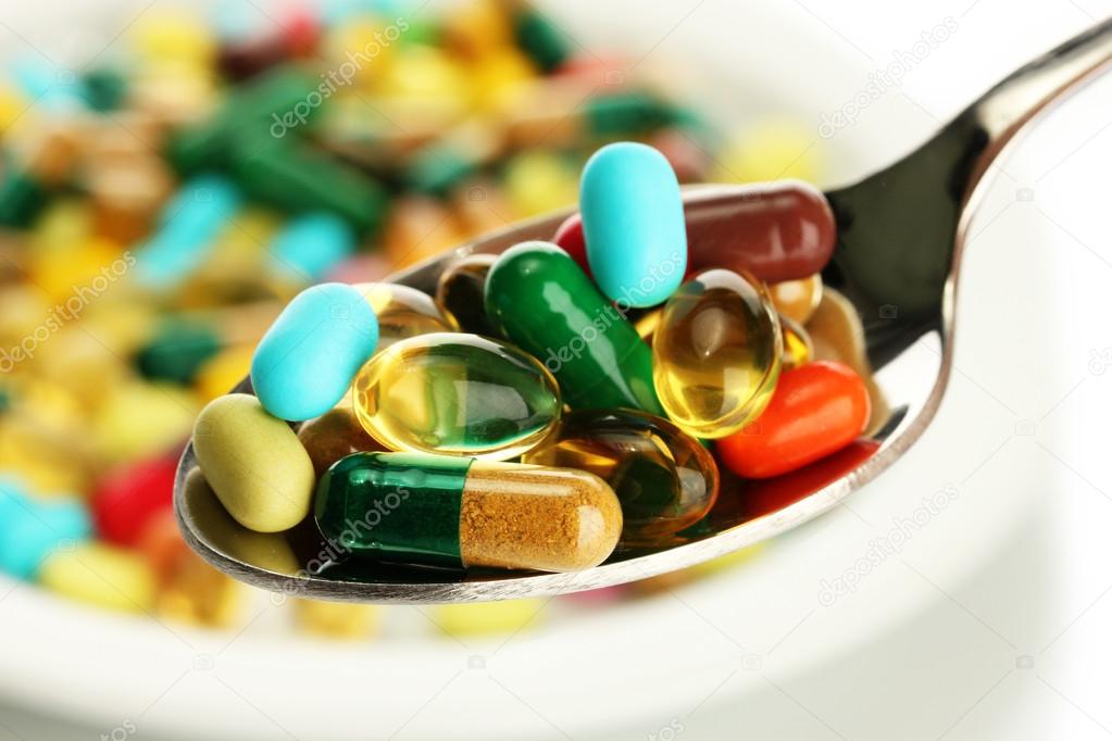 Colorful capsules and pills on plate with spoon, close up