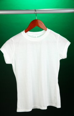 Askı üzerinde yeşil bir arka plan üzerinde beyaz t-shirt
