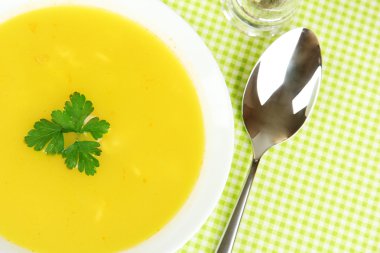 Yeşil masa örtüsü üzerinde beyaz tabak içinde kokulu çorba