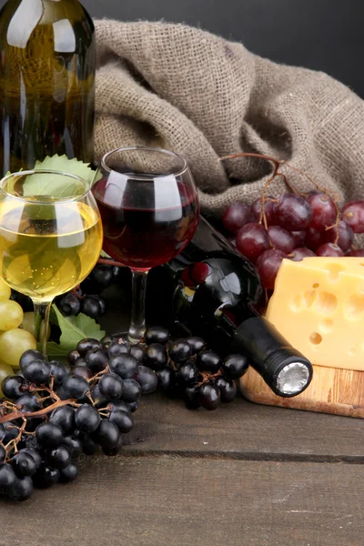 Flaschen und Gläser mit Wein, Käse und Trauben auf grauem Hintergrund — Stockfoto