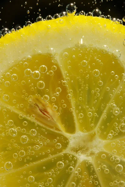 Rodaja de limón en el agua con burbujas, sobre fondo negro — Foto de Stock