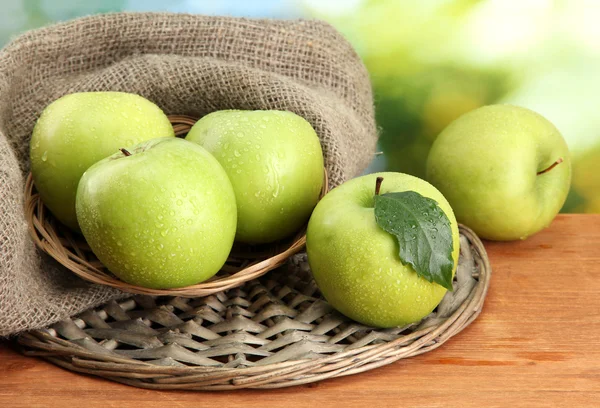 Reife grüne Äpfel im Korb auf Klette, auf Holztisch, auf grünem Hintergrund — Stockfoto