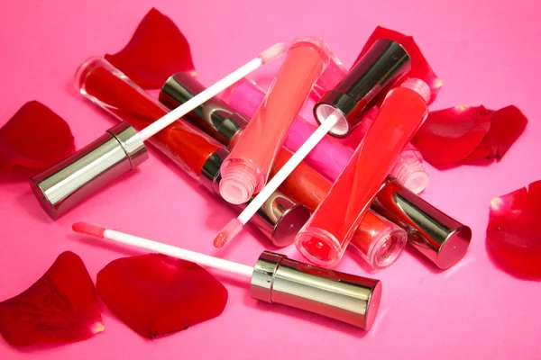 Beautiful lip glosses with rose petals, on pink background — Stock Photo, Image