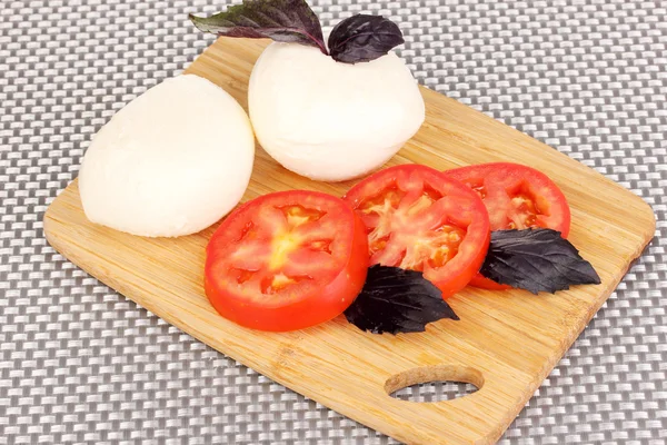 Doğrama kurulu mat üzerinde domates ile lezzetli Mozzarella peyniri — Stok fotoğraf