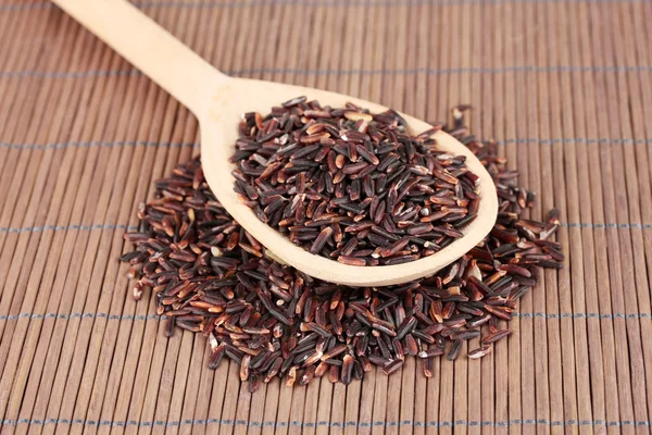 Black rice in wooden spoon on bamboo mat — Stock Photo, Image