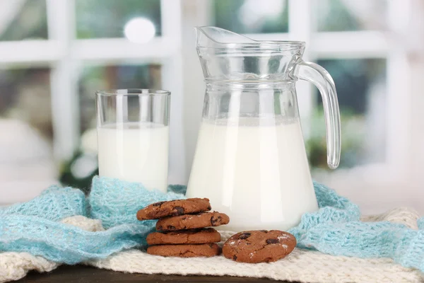 Jarro e copo de leite com biscoitos em malhas de pescoços de tripulação em mesa de madeira — Fotografia de Stock