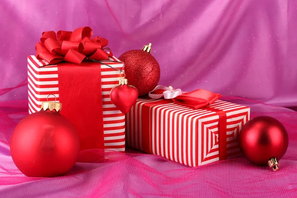 Coloridos regalos rojos con lazo y bolas de Navidad sobre fondo rosa — Foto de Stock