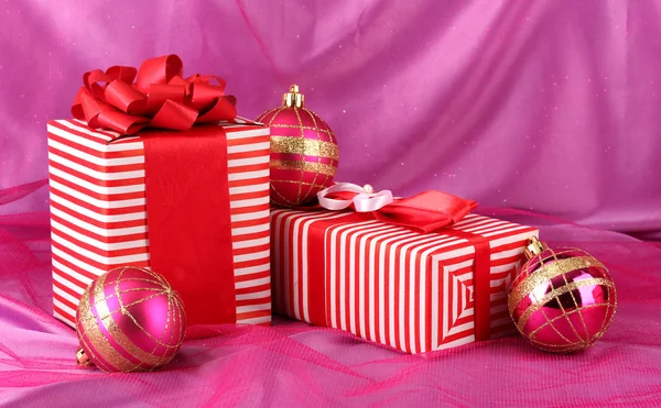 Pembe bir arka plan üzerinde yay ve Noel topları ile kırmızı renkli hediyeler — Stok fotoğraf
