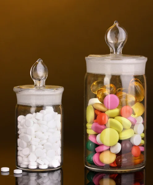 Capsules en pillen in recipiënten op oranje achtergrond — Stockfoto