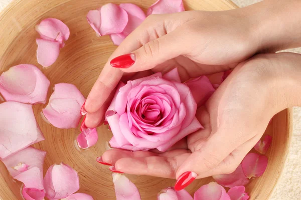 Manos de mujer con cuenco de madera de agua con pétalos — Foto de Stock