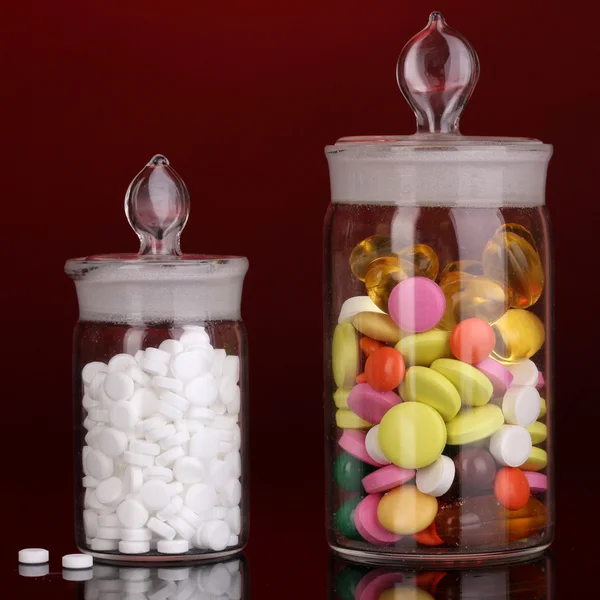 Cápsulas y pastillas en recipientes sobre fondo rojo —  Fotos de Stock