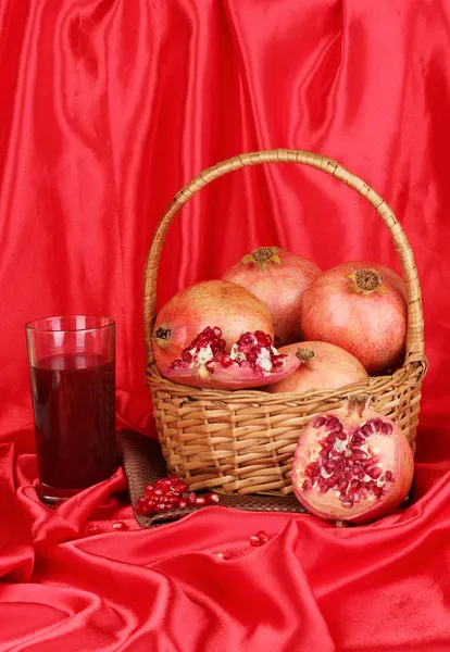 Zralé granátová jablka na košík s sklenici šťávy z granátového jablka na červenou látkou ba — Stock fotografie