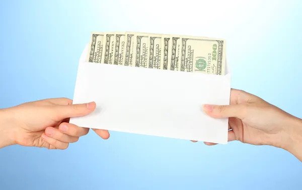 Kvinnans hand passerar kuvertet med lönen på blå bakgrund — Stockfoto